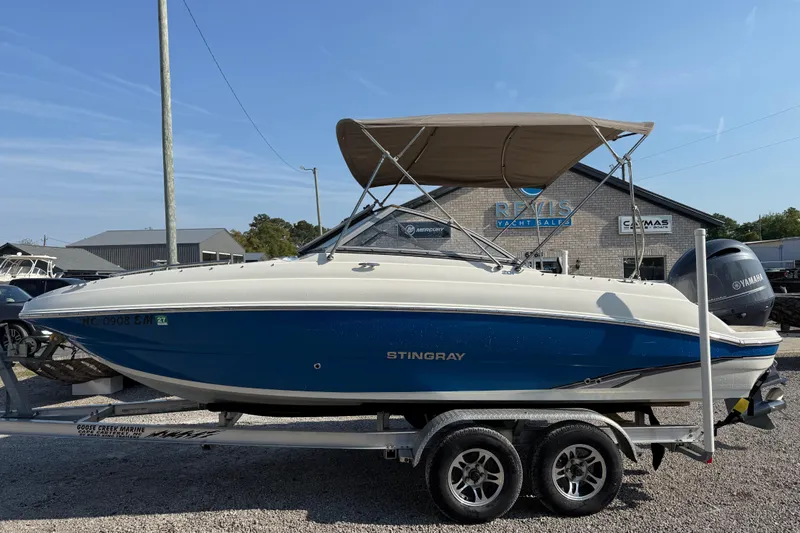 The Image of 2019 Stingray 201 DS boat on trailer, blue and white, with canopy, at yacht sales lot. - 1