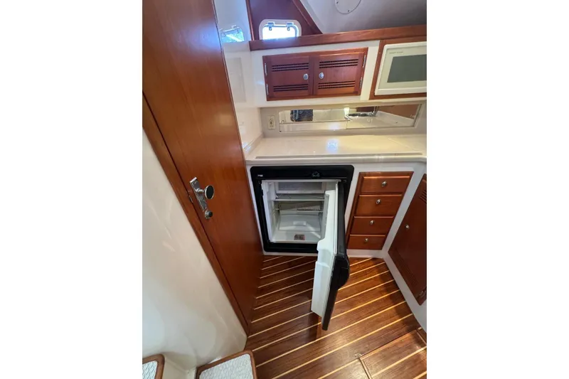 Slide: The Image of 1998 Cabo Yachts 35 Express interior with open fridge, wooden cabinets, and striped flooring. - 30