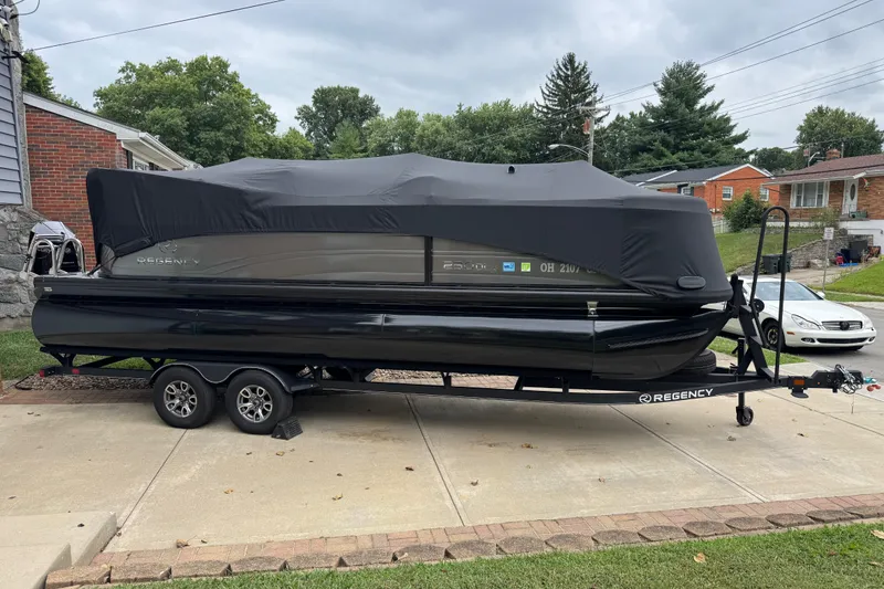 Slide: The Image of 2024 Regency 230 DL3 pontoon boat on trailer, covered, parked in driveway. - 3
