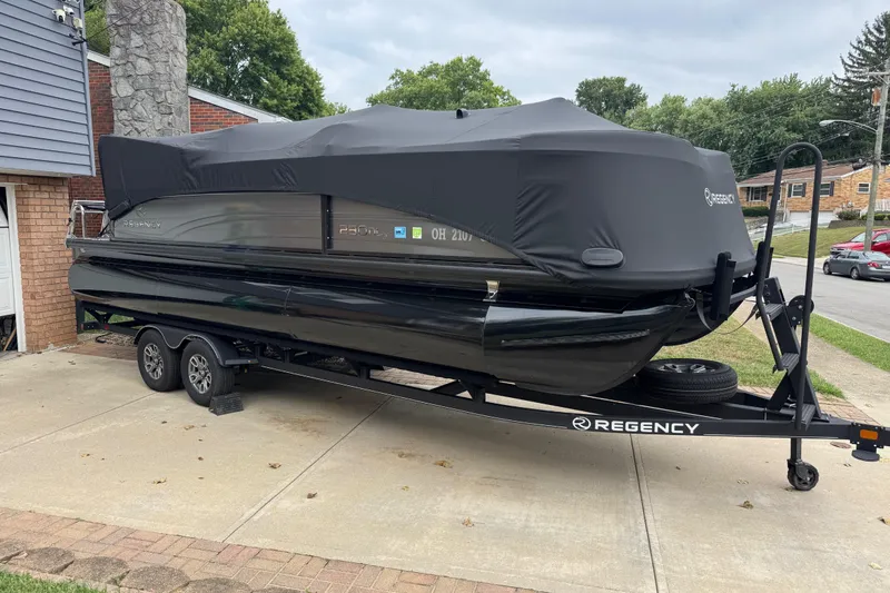 Slide: The Image of 2024 Regency 230 DL3 pontoon boat covered on trailer in residential driveway. - 45