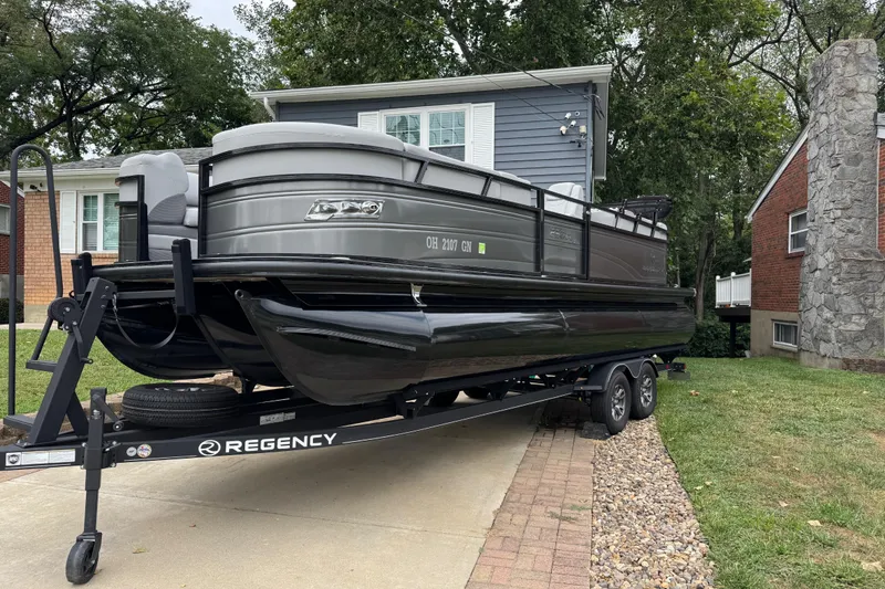 Slide: The Image of 2024 Regency 230 DL3 pontoon boat on trailer in residential driveway. - 5