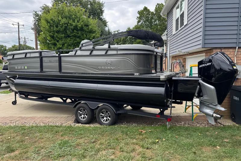 Slide: The Image of 2024 Regency 230 DL3 pontoon boat on trailer, parked in residential driveway. - 6