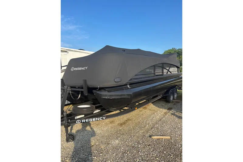 Slide: The Image of 2021 Regency 250 DL3 pontoon boat covered on a trailer, parked outdoors. - 7