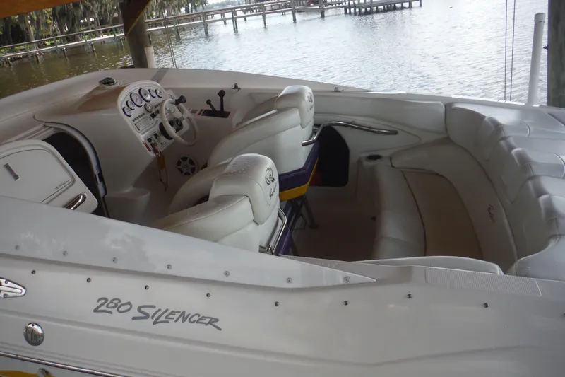 Slide: The Image of 2001 Powerquest 280 Silencer boat interior with white seating and dashboard, docked by the water. - 11