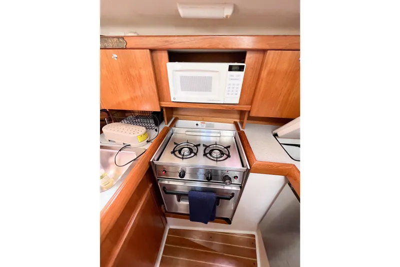 Slide: The Image of 2005 Catalina 350 yacht kitchen with stove, microwave, and wooden cabinetry. - 23