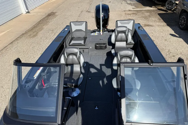 Slide: The Image of 2026 Lund 1875 Crossover XS boat with seating and windshield, parked on pavement. - 14