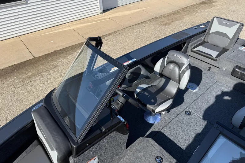 Slide: The Image of 2026 Lund 1875 Crossover XS boat interior with seating and windshield, parked on pavement. - 15