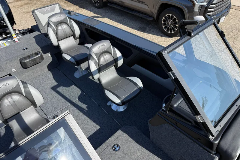 Slide: The Image of 2026 Lund 1875 Crossover XS boat interior with seating and windshield, parked beside a vehicle. - 19