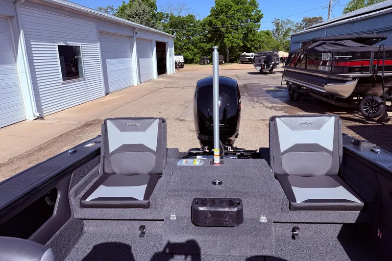 Slide: The Image of 2026 Lund 1875 Crossover XS boat interior with seating and motor, parked outside a garage. - 26