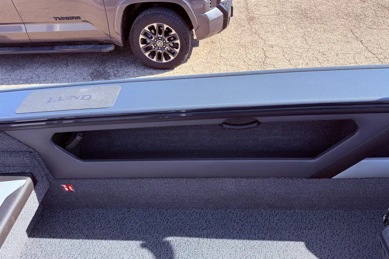 Slide: The Image of 2026 Lund 1875 Crossover XS boat interior with storage compartment, parked beside a truck. - 33