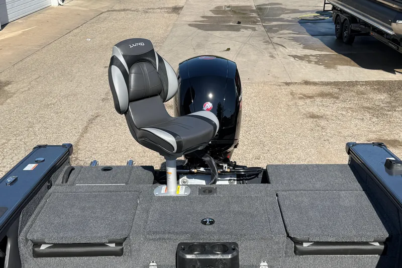 Slide: The Image of 2026 Lund 1875 Crossover XS boat interior with seat and motor, parked on concrete. - 34