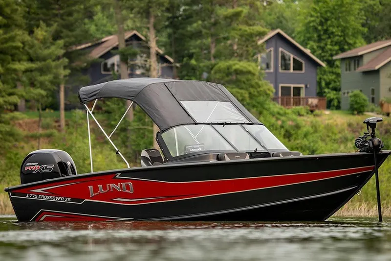 Slide: The Image of Manufacturer Provided Image: 2026 Lund 1875 Crossover XS boat on a lake, surrounded by trees and houses. - 5