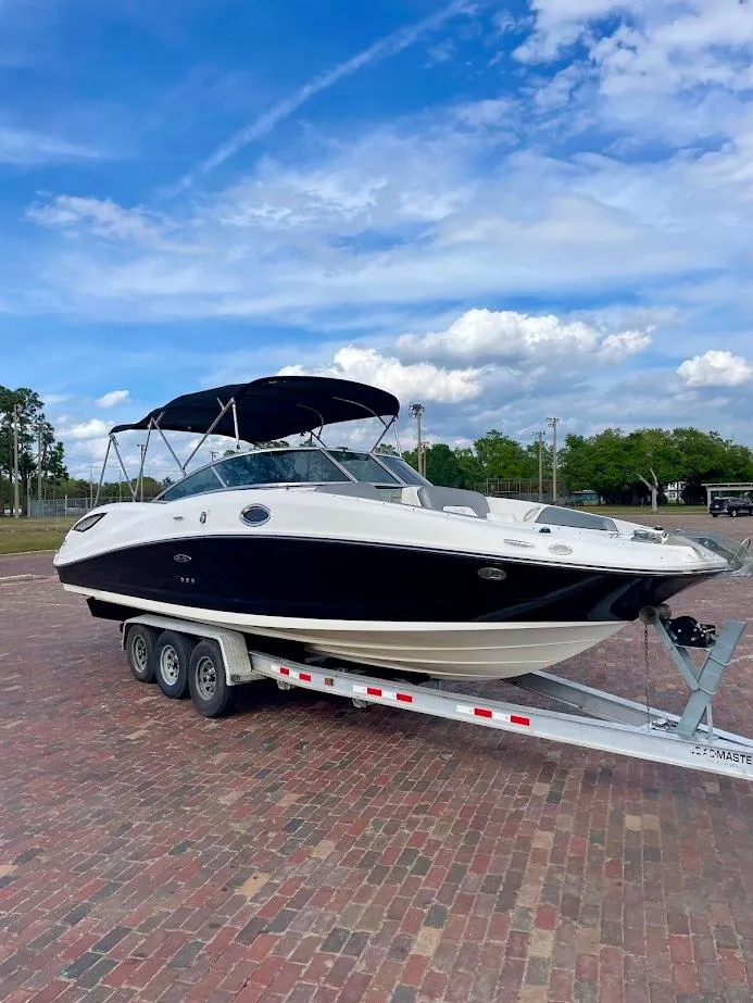 The Image of 2010 Sea Ray 300 Sundeck boat on trailer, parked on brick pavement under blue sky. - 1
