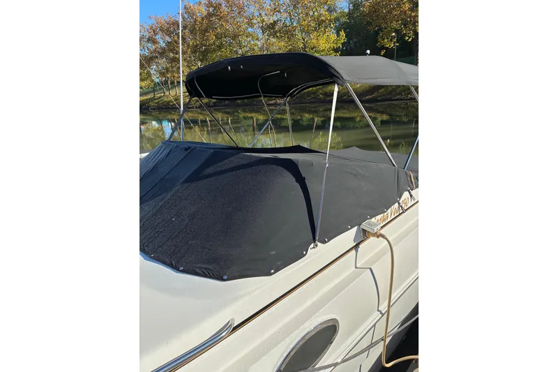 Slide: The Image of 2002 Rinker Fiesta Vee 250 boat with black canopy and cover, docked by a river. - 19