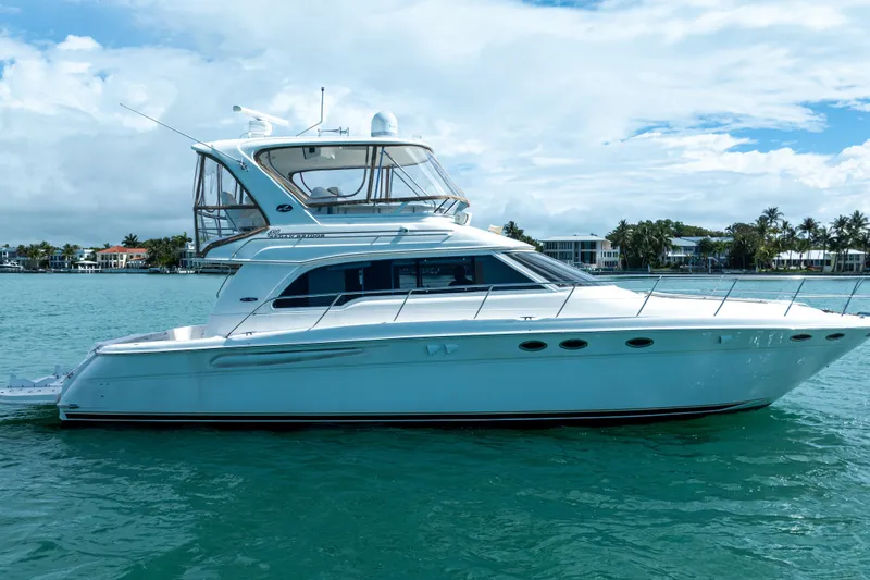 Slide: The Image of 2003 Sea Ray 480 Sedan Bridge yacht on calm water, with coastal homes in the background. - 5