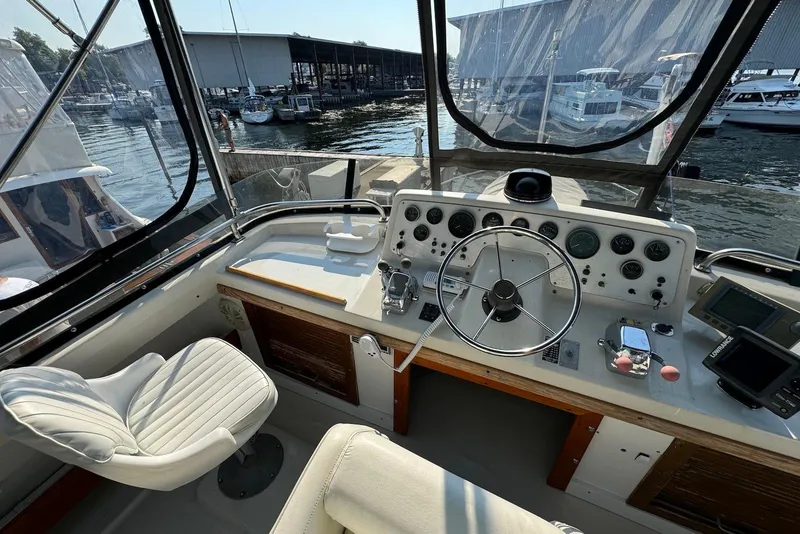 Slide: The Image of 1985 Silverton 40 Aft Cabin helm with steering wheel, gauges, and marina view. - 4