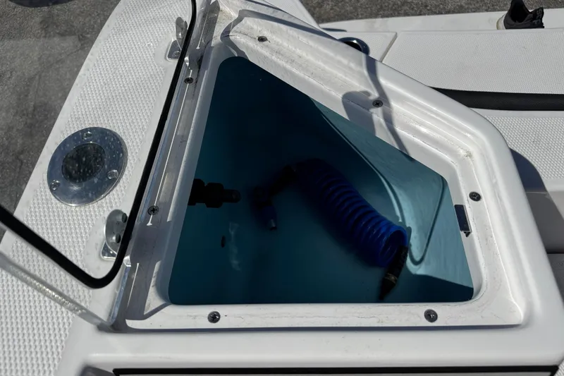 Slide: The Image of Open storage compartment on 2025 Yamaha Boats 222 FSH Sport, featuring a coiled hose. - 16