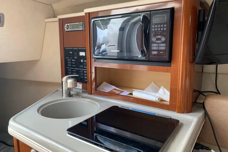 Slide: The Image of 2011 Sea Ray 240 Sundancer kitchenette with microwave, sink, and control panel. - 20