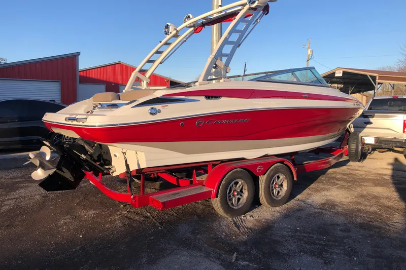 Slide: The Image of 2020 Crownline 235 SS boat in red and white on a trailer, parked outdoors. - 20
