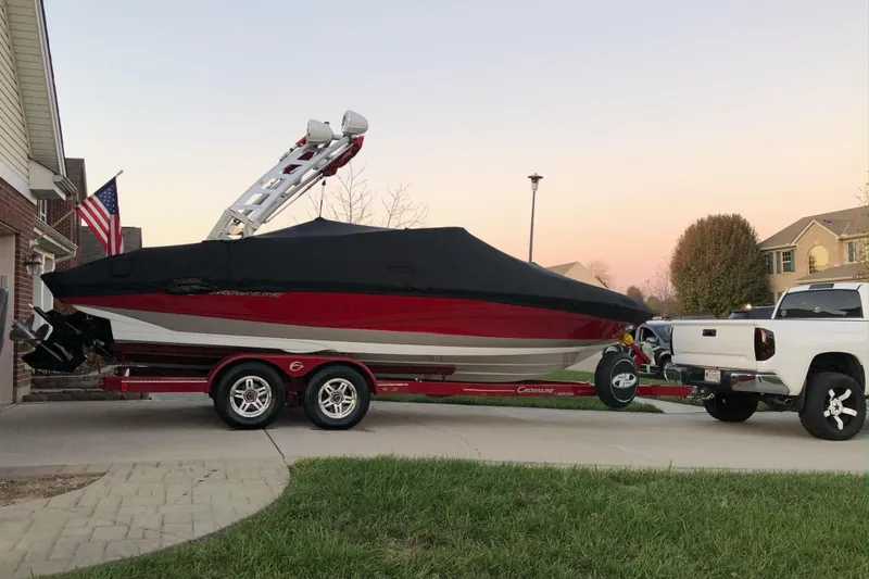 Slide: The Image of 2020 Crownline 235 SS boat on trailer, covered, parked in driveway at sunset. - 5