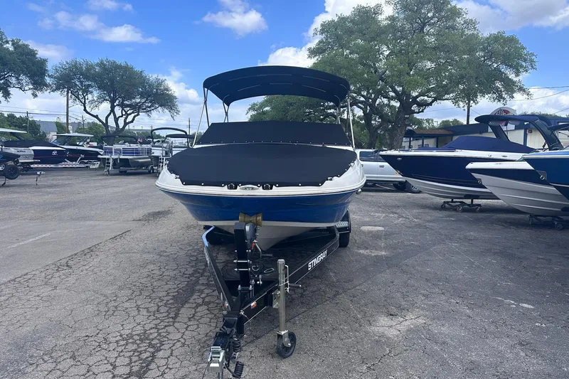 Slide: The Image of 2022 Stingray 201 DC boat on trailer, parked outdoors under a clear blue sky. - 2