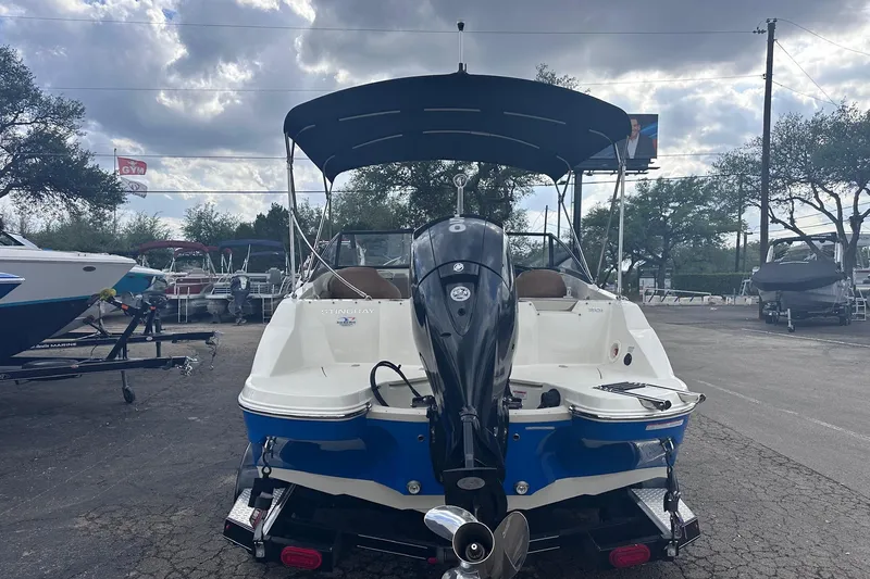 Slide: The Image of 2022 Stingray 201 DC boat with outboard motor and canopy, parked outdoors. - 4