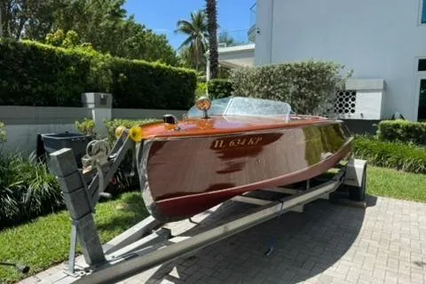 The Image of 1952 Chris-Craft 18 Runabout boat on trailer, parked outdoors in a sunny setting. - 0