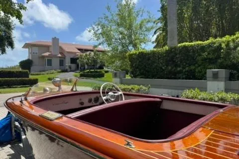 Slide: The Image of 1952 Chris-Craft 18 Runabout boat with wooden finish, parked near a modern house. - 13