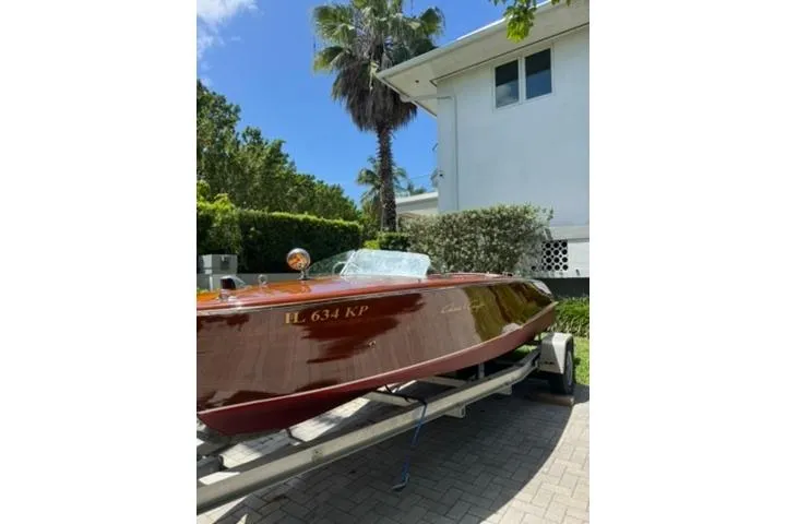 Slide: The Image of 1952 Chris-Craft 18 Runabout boat on trailer, parked near a house with palm trees. - 2