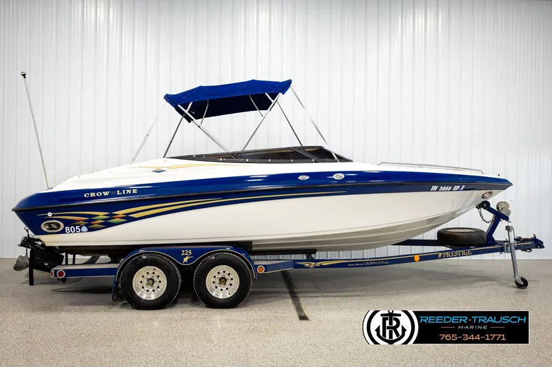 Slide: The Image of 2001 Crownline 225 BR boat with blue accents on a trailer in a showroom. - 5