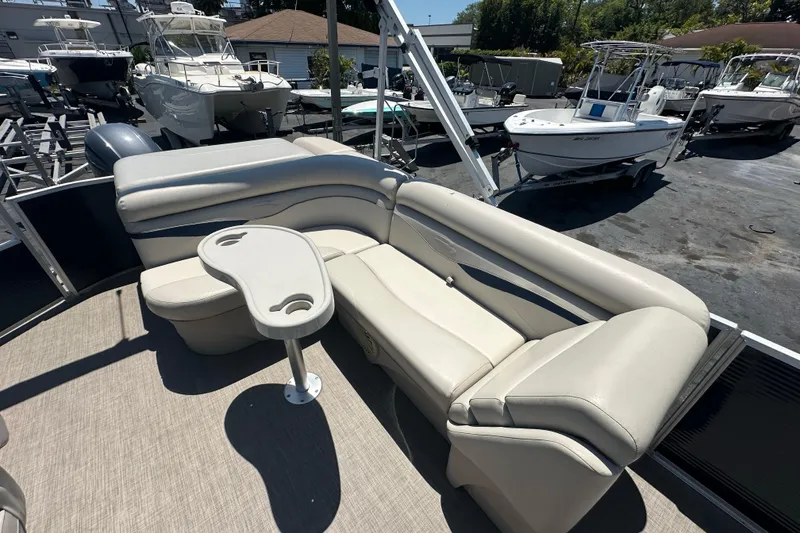 Slide: The Image of 2016 Bennington 21 SX L-Bench pontoon boat with beige seating and table, docked at marina. - 10