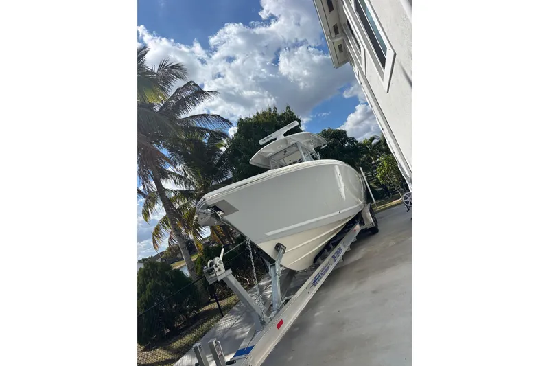 Slide: The Image of 2021 Cobia 320 Center Console boat on trailer, parked beside a house with palm trees. - 12