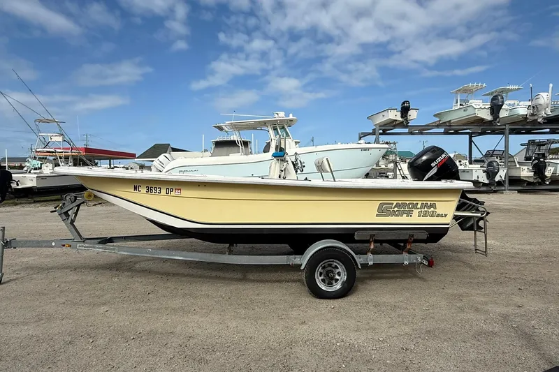 Slide: The Image of 2009 Carolina Skiff 198 DLV boat on trailer, parked in a marina under a blue sky. - 3