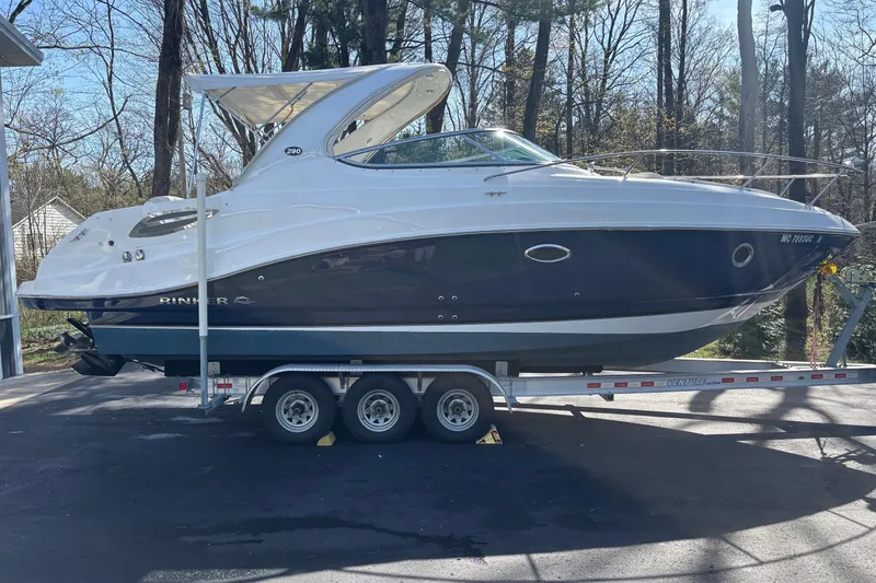 The Image of 2014 Rinker 290 Express Cruiser on trailer in wooded area. - 1