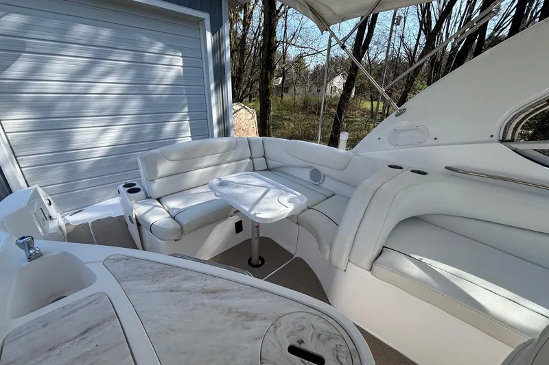 Slide: The Image of 2014 Rinker 290 Express Cruiser interior with white seating and table, docked near trees. - 13