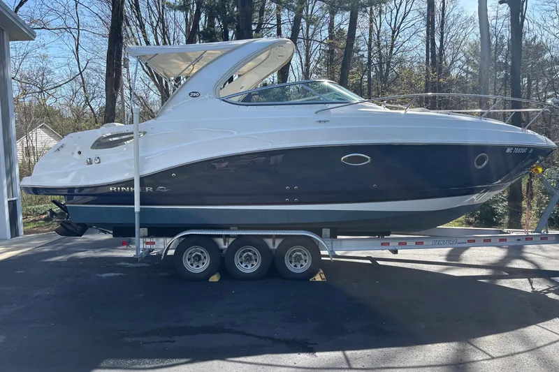 Slide: The Image of 2014 Rinker 290 Express Cruiser on trailer, parked outdoors, surrounded by trees. - 36