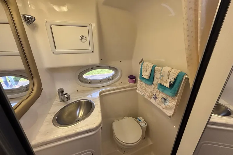 Slide: The Image of 2014 Rinker 290 Express Cruiser bathroom with sink, toilet, and porthole window. - 5