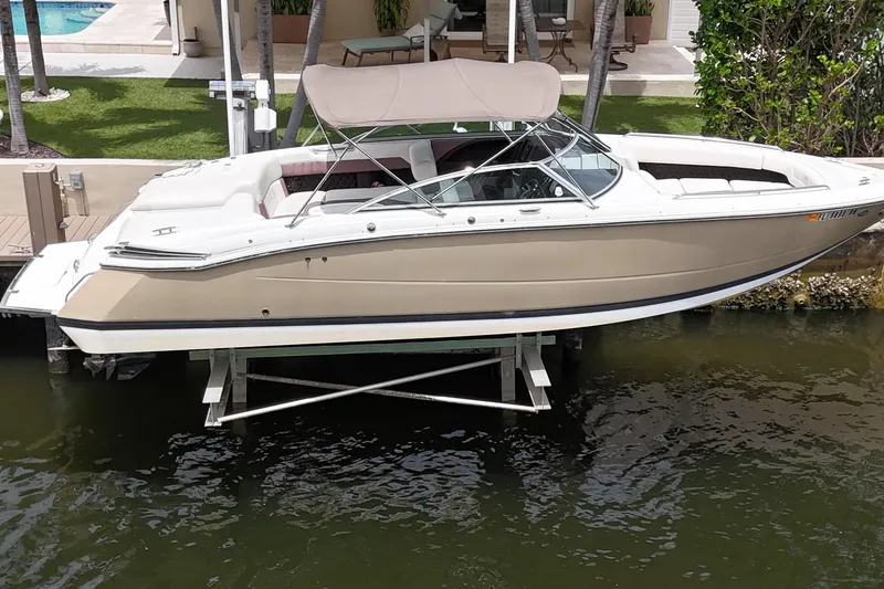 Slide: The Image of 2013 Cobalt 296 boat docked on lift, beige exterior, canopy, waterfront setting. - 2