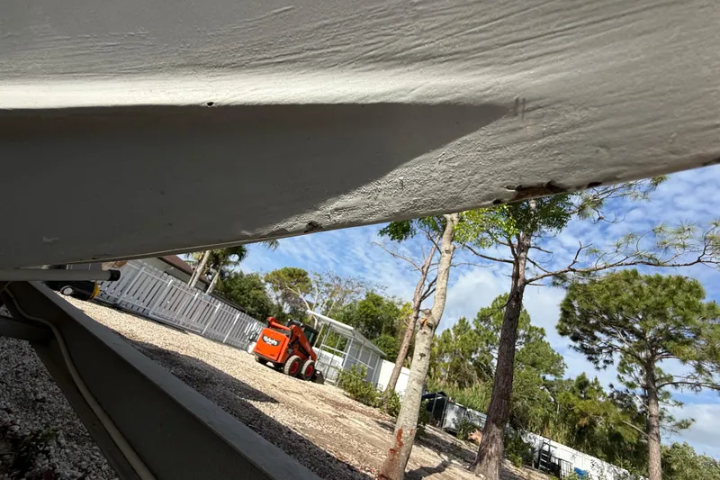 Slide: The Image of 1989 Wellcraft 302 Scarab boat hull with visible wear, parked outdoors near trees. - 121