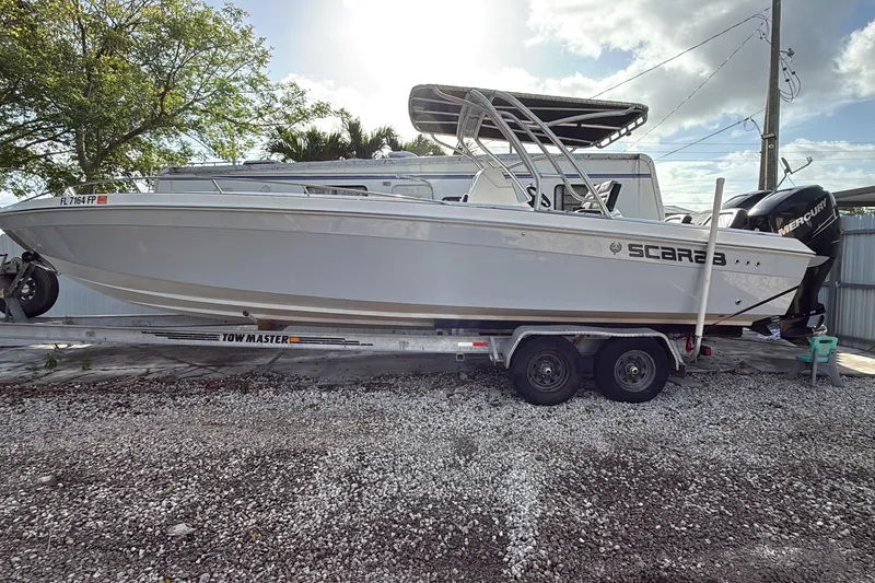 Slide: The Image of 1989 Wellcraft 302 Scarab boat on trailer, parked outdoors under a cloudy sky. - 128
