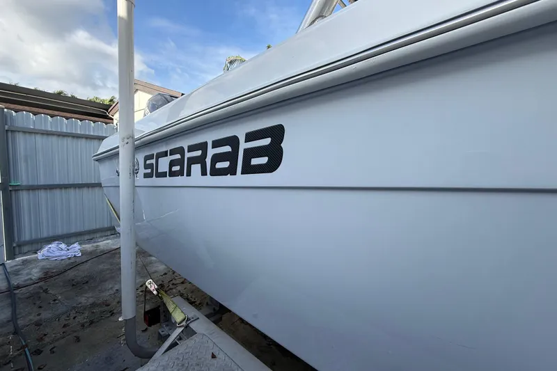 Slide: The Image of 1989 Wellcraft 302 Scarab boat side view with logo, parked in a fenced area. - 37