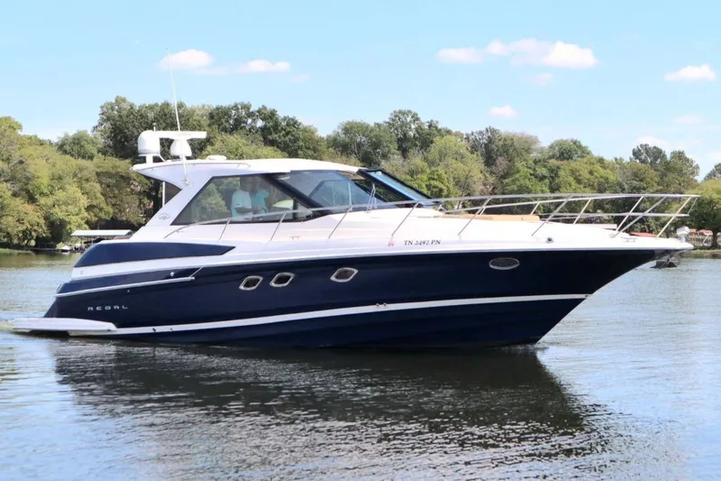 Slide: The Image of 2010 Regal 46 Sport Coupe yacht cruising on a serene lake with lush greenery. - 3