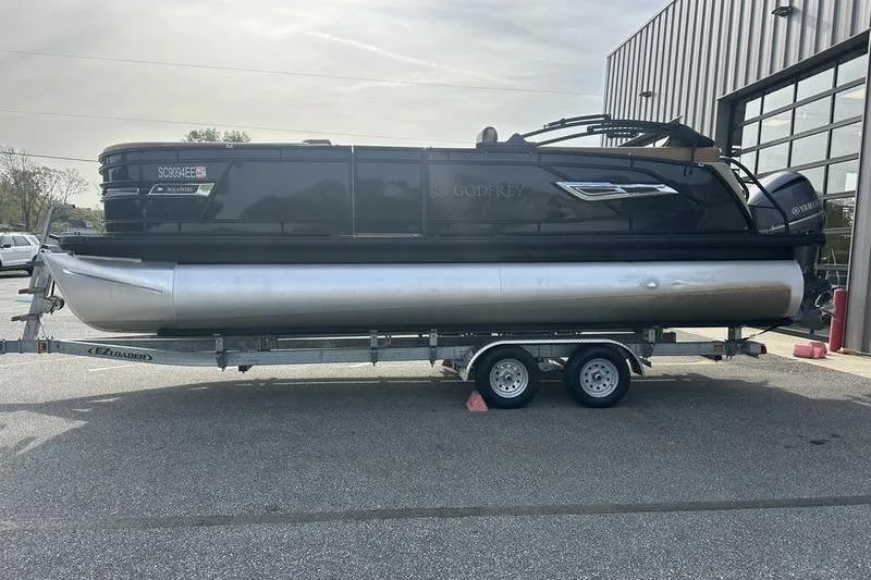 The Image of 2024 Godfrey AquaPatio 235 ULC iMPACT pontoon boat on trailer outside building. - 0