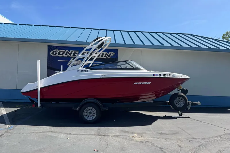 The Image of 2024 Yamaha Boats AR190 in red, parked on a trailer outside a building. - 1