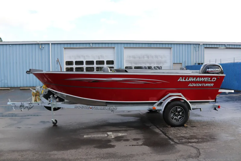 The Image of 2026 Alumaweld Adventurer 18 boat on trailer, red exterior, parked outside industrial building. - 0