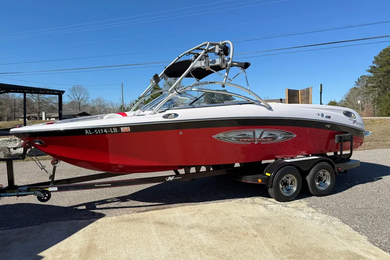 The Image of 2004 Nautique Air Nautique 226 boat on trailer, red and white design, parked outdoors. - 1