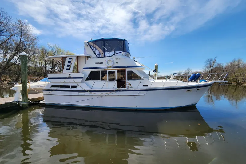 The Image of 1987 Jefferson 42 SE Sundeck Motor Yacht docked on a calm river under a clear sky. - 0