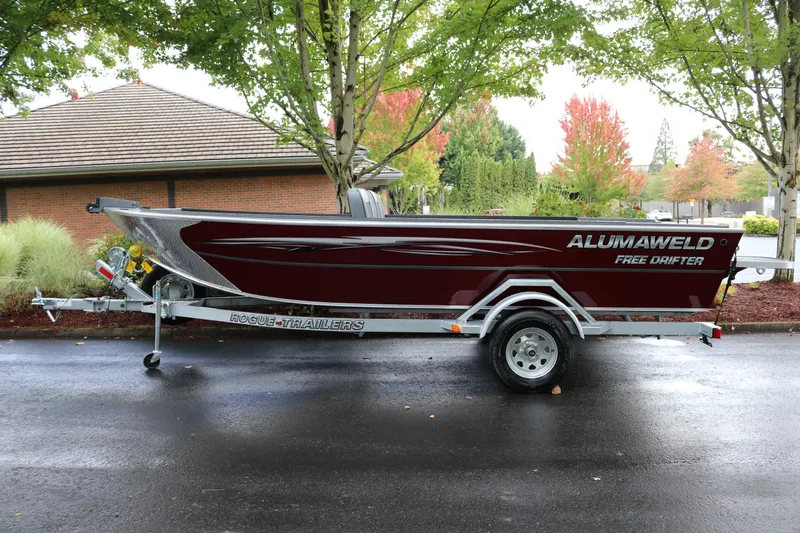 The Image of 2026 Alumaweld Free Drifter 18 boat on trailer, parked outdoors with trees in background. - 0