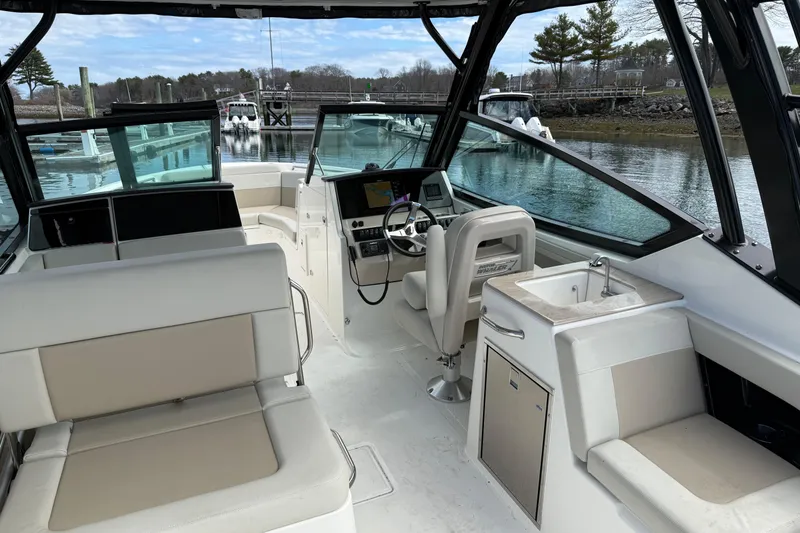 Slide: The Image of 2023 Boston Whaler 280 Vantage boat interior with seating and helm, docked by the water. - 2