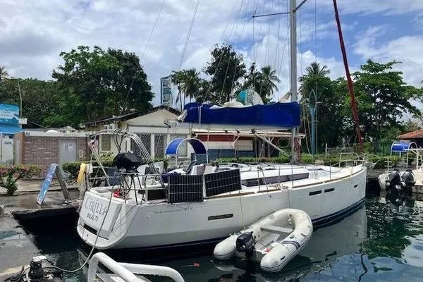 Slide: The Image of 2018 Jeanneau Sun Odyssey 419 sailboat docked with inflatable dinghy, surrounded by lush greenery. - 16